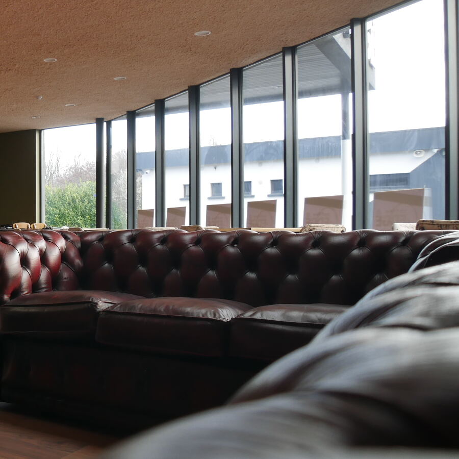 Tall glazed windows and a leather Chesterfield sofa, looking out to the car park.