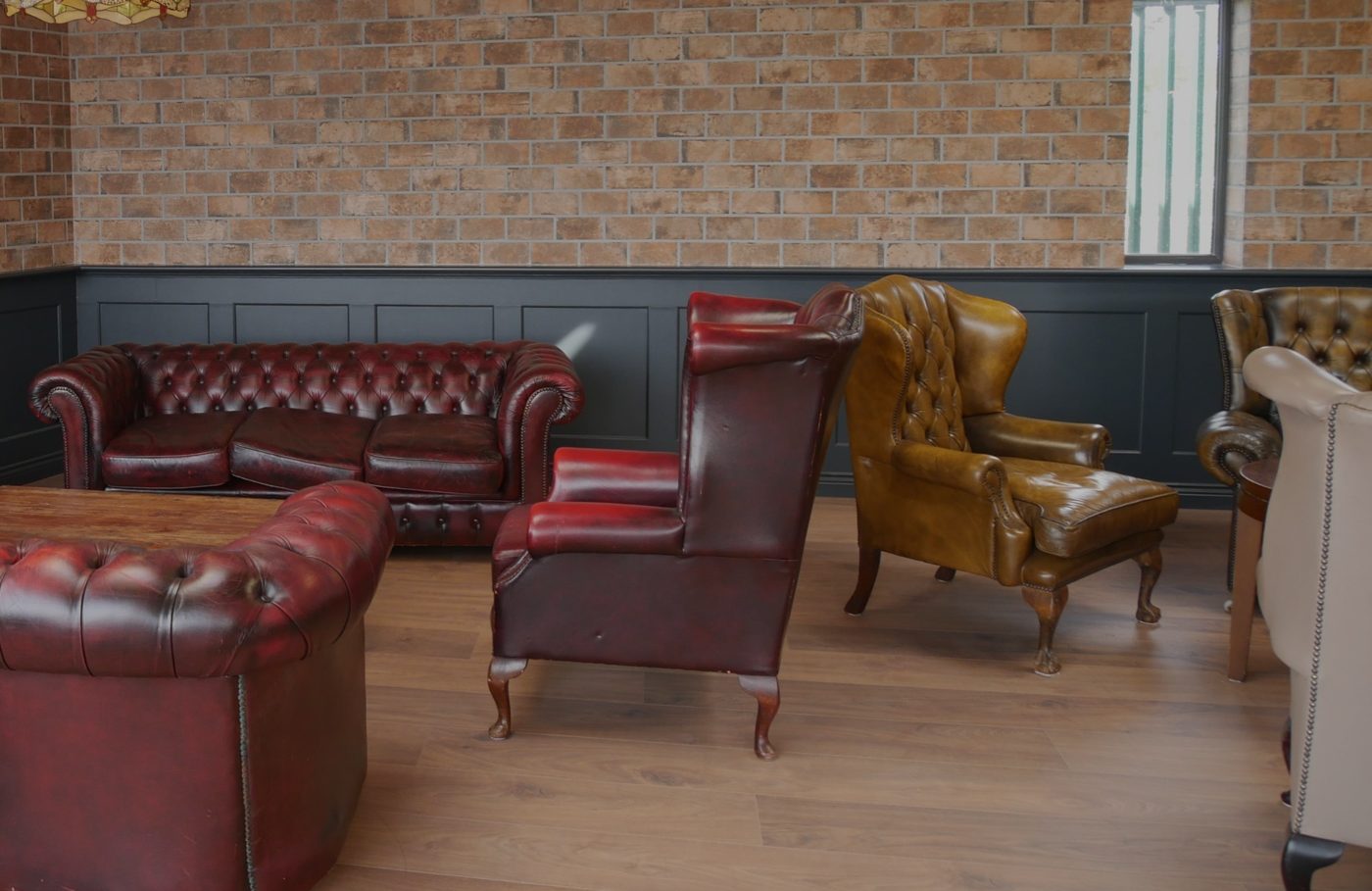 The brick-walled lounge: leather sofas, a tan wingback chair and dark panelling.