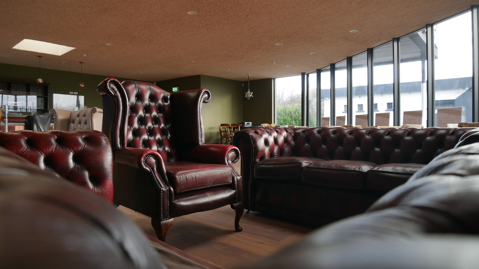 Oxblood leather armchair and Chesterfield sofa in the café, with tall glazed windows on the right.